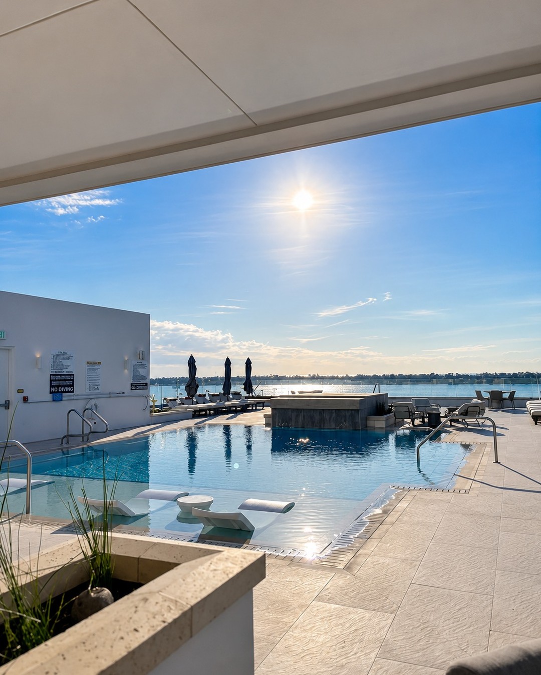 Modern waterfront pool deck with in-water loungers and a raised water feature facing open water