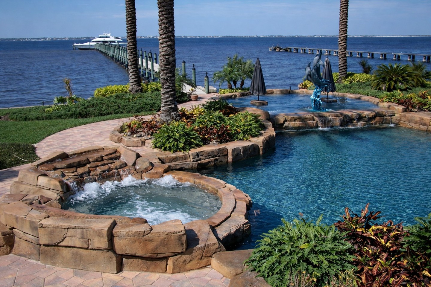 Round rock spa with a stone spillway next to a freeform pool overlooking the waterfront